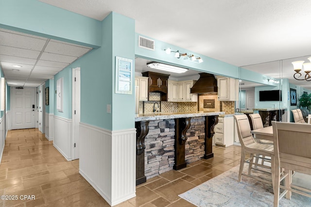 kitchen with sink, a drop ceiling, a breakfast bar area, decorative backsplash, and premium range hood