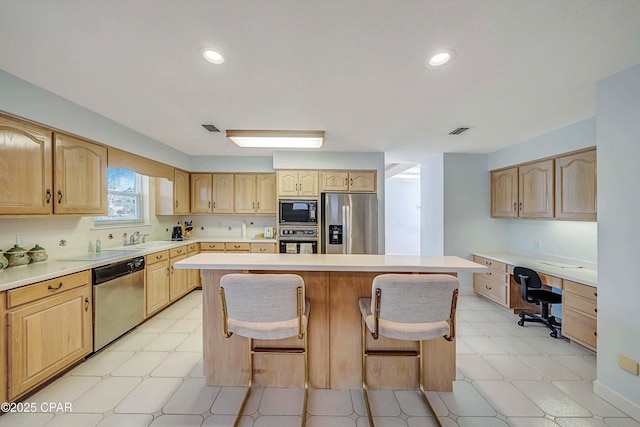 kitchen featuring a kitchen island, built in desk, a kitchen breakfast bar, black appliances, and light brown cabinets