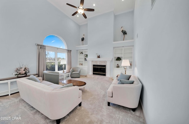 living room with high vaulted ceiling, light carpet, built in features, ceiling fan, and a high end fireplace