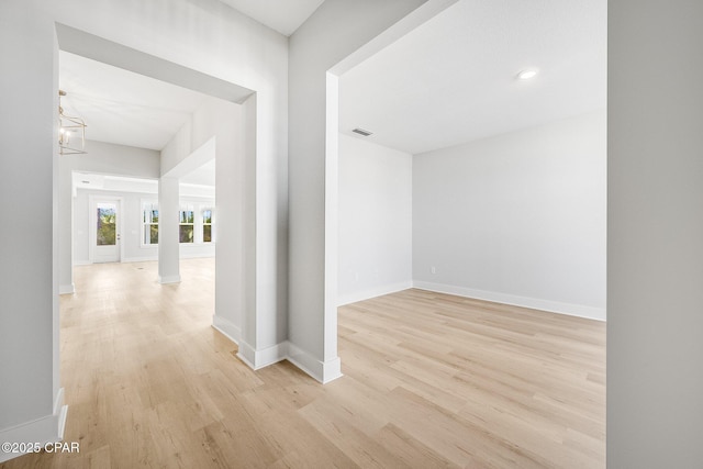 corridor featuring a chandelier, decorative columns, and light hardwood / wood-style flooring