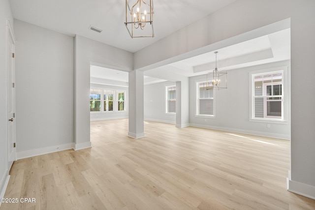 empty room featuring a raised ceiling, a chandelier, and light hardwood / wood-style flooring