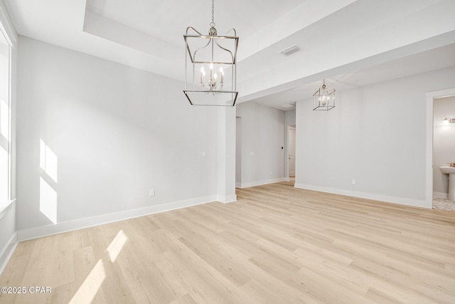 interior space with an inviting chandelier, a tray ceiling, and light hardwood / wood-style floors