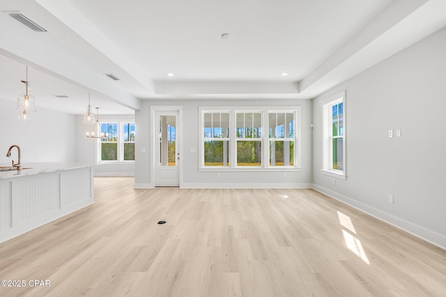 unfurnished living room featuring an inviting chandelier, a raised ceiling, sink, and light hardwood / wood-style flooring