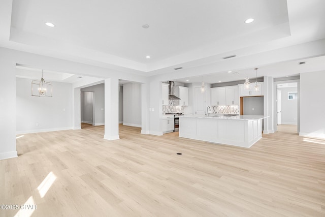 unfurnished living room with sink, a chandelier, light hardwood / wood-style floors, and a tray ceiling