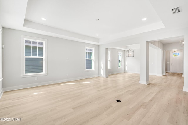 unfurnished living room featuring a notable chandelier, a tray ceiling, and light wood-type flooring