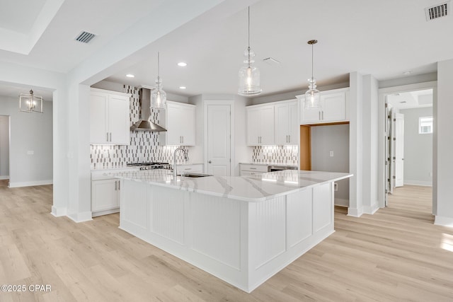 kitchen featuring wall chimney range hood, white cabinets, and a spacious island