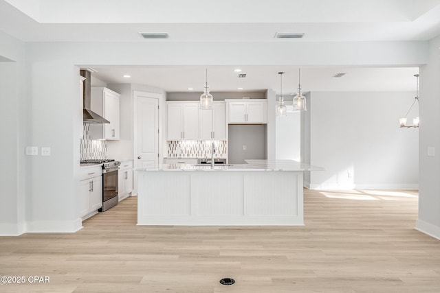 kitchen with stainless steel range with gas cooktop, a center island with sink, white cabinets, and decorative light fixtures