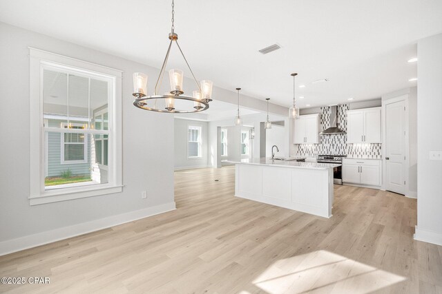 kitchen with pendant lighting, white cabinetry, a kitchen island with sink, stainless steel range oven, and wall chimney exhaust hood