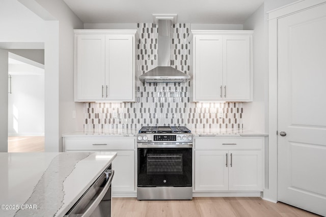 kitchen with wall chimney range hood, stainless steel appliances, white cabinets, and light stone countertops