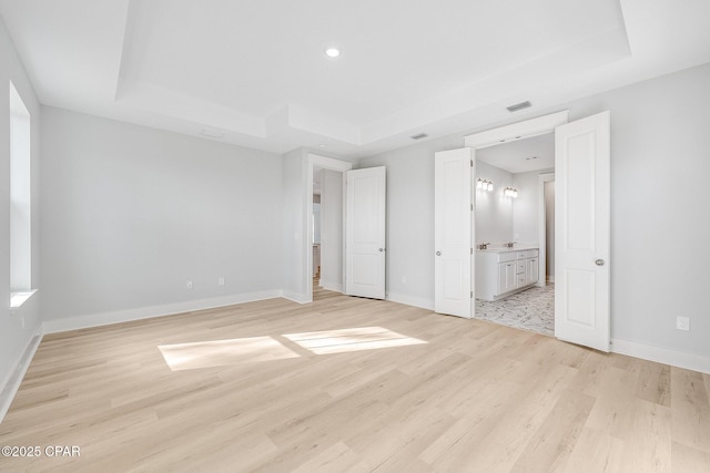 unfurnished bedroom featuring a raised ceiling, ensuite bathroom, and light hardwood / wood-style flooring