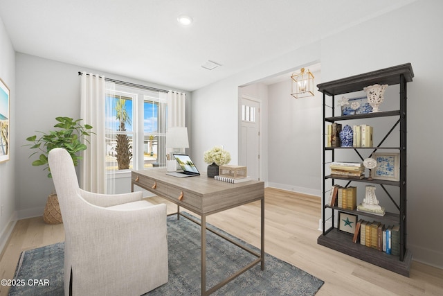 home office with an inviting chandelier and light hardwood / wood-style flooring