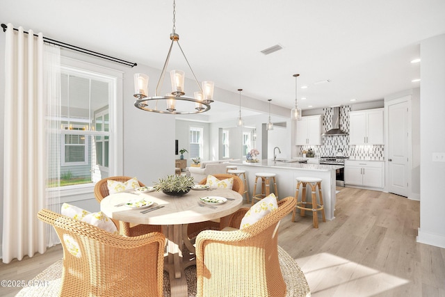 dining area with sink, a notable chandelier, and light wood-type flooring