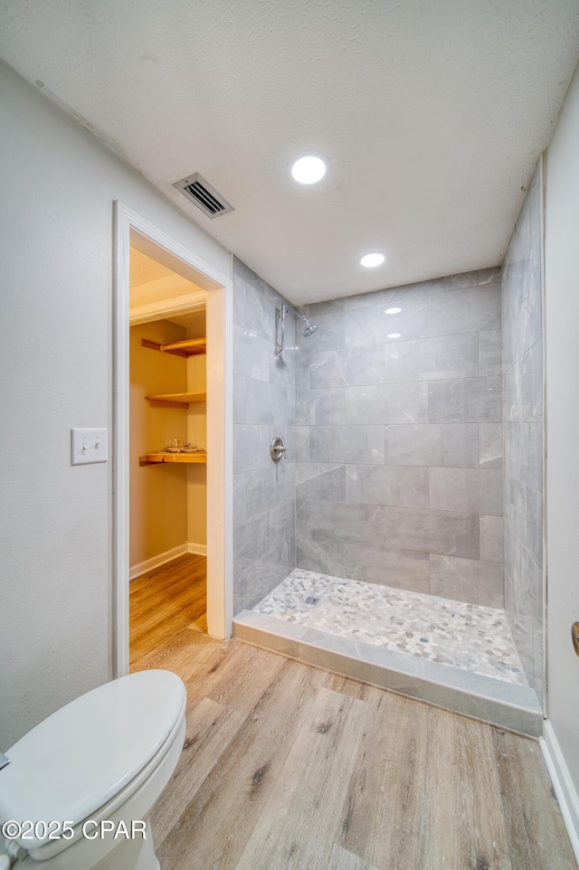 bathroom with hardwood / wood-style floors, tiled shower, and toilet