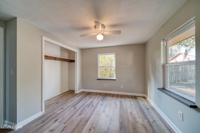 unfurnished bedroom with light hardwood / wood-style floors, ceiling fan, a closet, a textured ceiling, and multiple windows