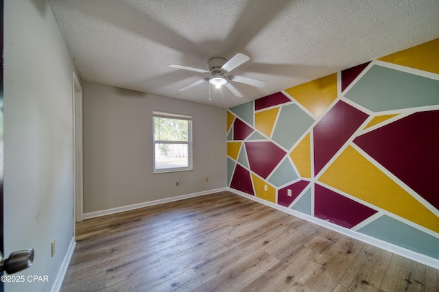 empty room with ceiling fan, wood-type flooring, and a textured ceiling