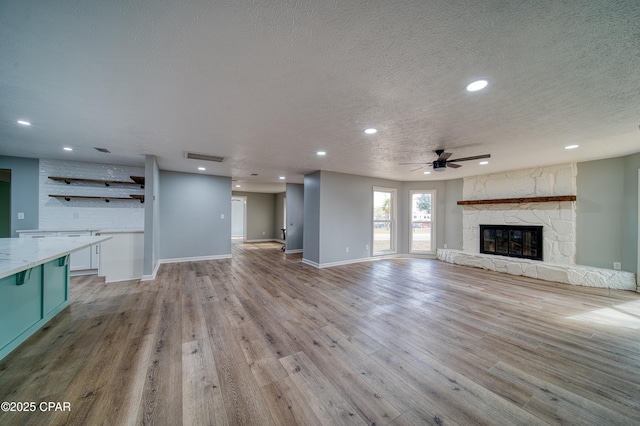 unfurnished living room with a textured ceiling, ceiling fan, light hardwood / wood-style floors, and a stone fireplace