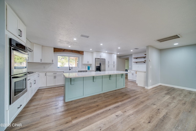 kitchen with stainless steel appliances, a center island, a textured ceiling, white cabinets, and sink