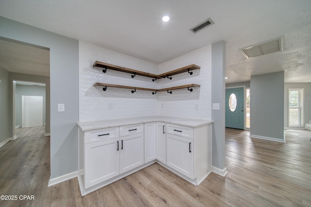 kitchen featuring a textured ceiling, white cabinetry, tasteful backsplash, and light wood-type flooring