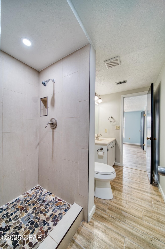 bathroom with a textured ceiling, toilet, vanity, and a tile shower