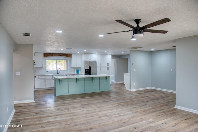 kitchen featuring tasteful backsplash, a center island, a textured ceiling, white cabinets, and stainless steel fridge