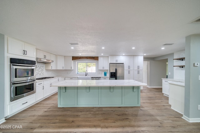 kitchen featuring white cabinets, appliances with stainless steel finishes, light stone counters, and a center island