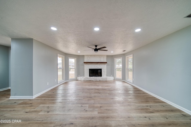 unfurnished living room featuring light hardwood / wood-style floors, a textured ceiling, ceiling fan, and a fireplace