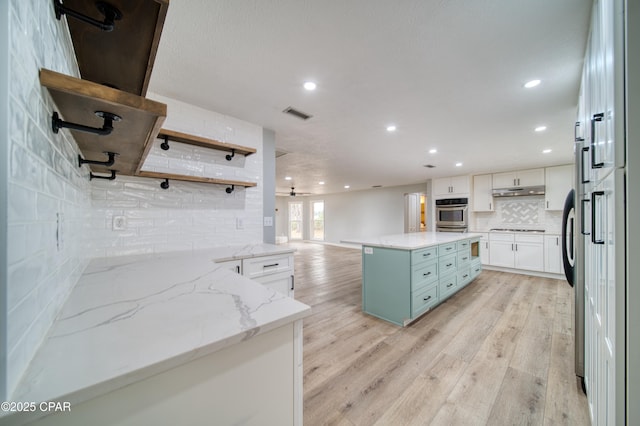 kitchen featuring light stone countertops, a center island, white cabinetry, decorative backsplash, and light hardwood / wood-style floors