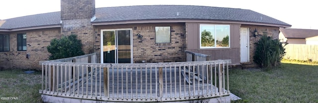 exterior space with brick siding, a chimney, a front yard, fence, and a wooden deck