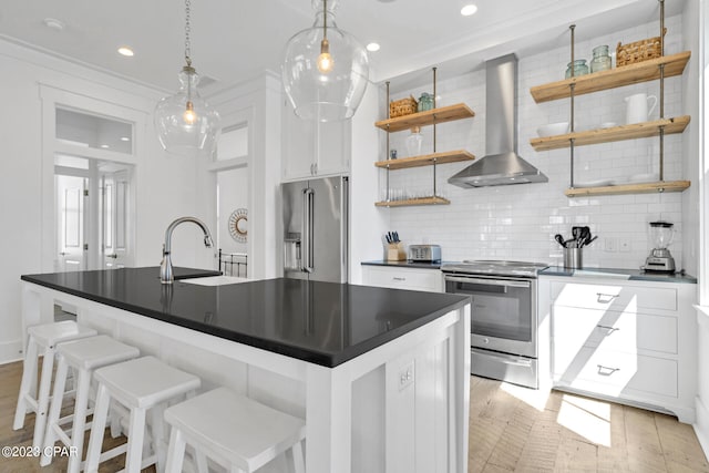 kitchen with hanging light fixtures, stainless steel appliances, wall chimney range hood, backsplash, and white cabinetry