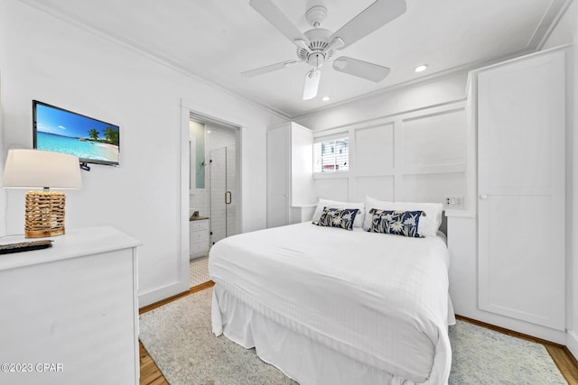 bedroom featuring ceiling fan, light hardwood / wood-style flooring, ornamental molding, and ensuite bath