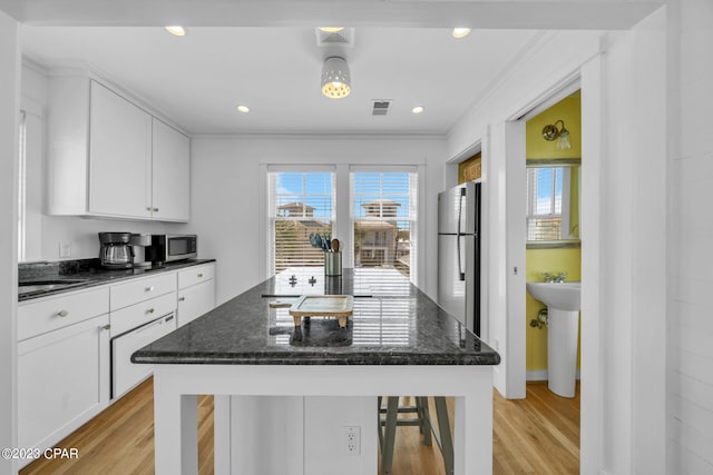 kitchen featuring white cabinets, appliances with stainless steel finishes, dark stone countertops, and light hardwood / wood-style flooring