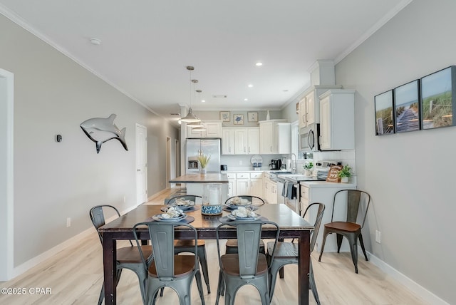 dining area featuring sink, light wood-type flooring, and crown molding