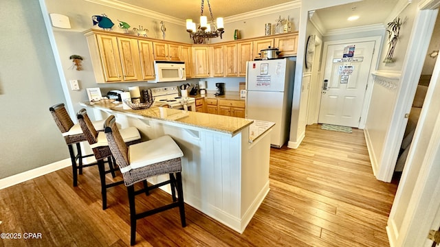 kitchen featuring an inviting chandelier, a kitchen bar, kitchen peninsula, white appliances, and light stone countertops