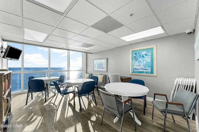 dining room featuring dark wood-type flooring, floor to ceiling windows, and a drop ceiling