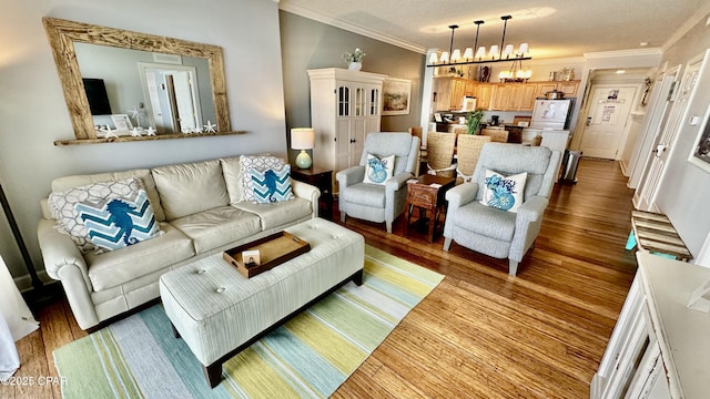 living room featuring a chandelier, a textured ceiling, ornamental molding, and light hardwood / wood-style floors