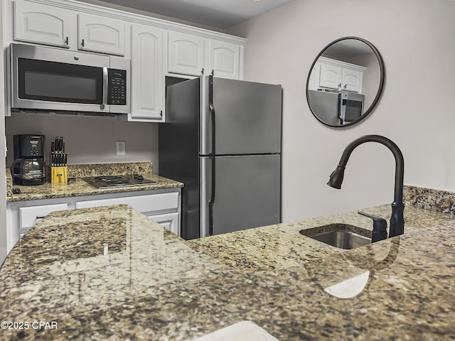 kitchen with white cabinetry, appliances with stainless steel finishes, sink, and dark stone countertops