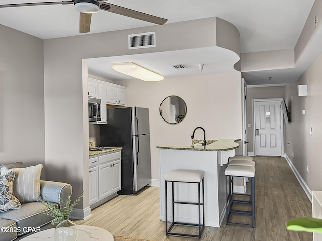 kitchen featuring white cabinetry, a breakfast bar area, stainless steel appliances, light stone countertops, and light wood-type flooring