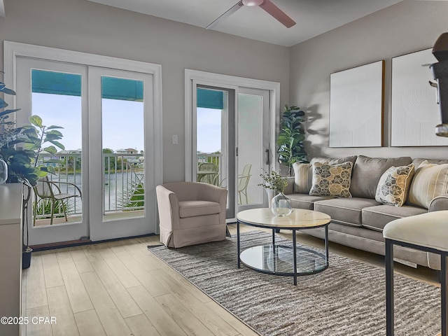 living room featuring ceiling fan, a water view, and light wood-type flooring