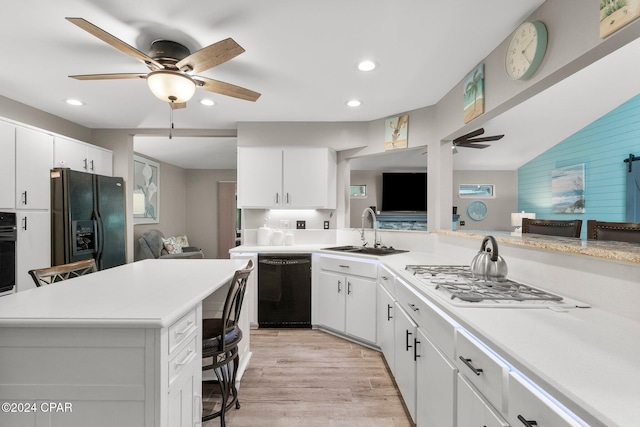 kitchen featuring sink, a breakfast bar area, white cabinets, and black appliances