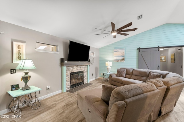 living room with light hardwood / wood-style floors, vaulted ceiling, a barn door, and a fireplace