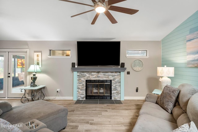 living room featuring french doors, light hardwood / wood-style floors, lofted ceiling, ceiling fan, and a stone fireplace