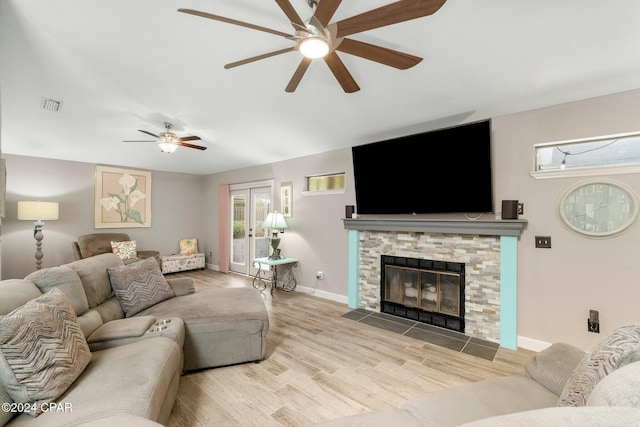 living room with light wood-type flooring, ceiling fan, and a stone fireplace