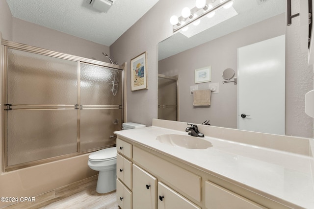 full bathroom featuring vanity, a textured ceiling, hardwood / wood-style floors, toilet, and combined bath / shower with glass door