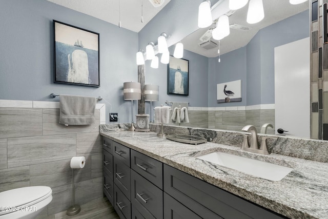 bathroom featuring a textured ceiling, tile walls, ceiling fan, toilet, and vanity