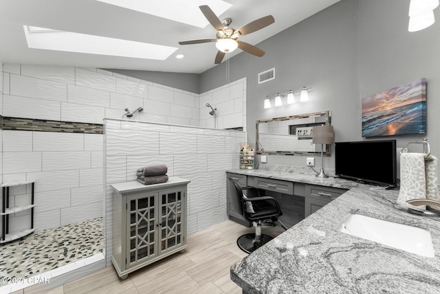 bathroom with tiled shower, tile walls, ceiling fan, vanity, and lofted ceiling with skylight