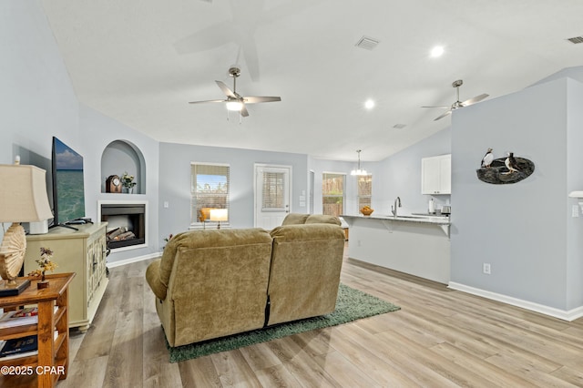 living room with sink, vaulted ceiling, light wood-type flooring, a chandelier, and built in shelves