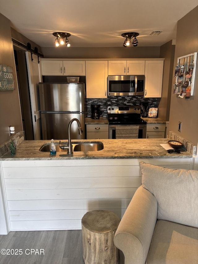 kitchen featuring light stone countertops, a barn door, backsplash, white cabinetry, and appliances with stainless steel finishes