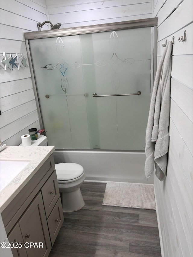 full bathroom featuring vanity, wood walls, hardwood / wood-style floors, and enclosed tub / shower combo