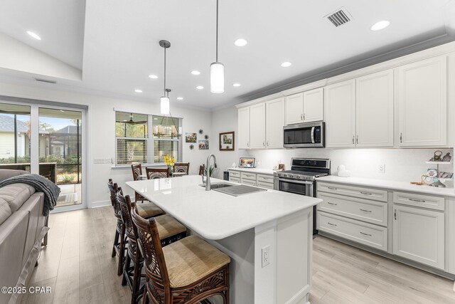 kitchen with hanging light fixtures, stainless steel appliances, a center island with sink, a breakfast bar area, and white cabinetry