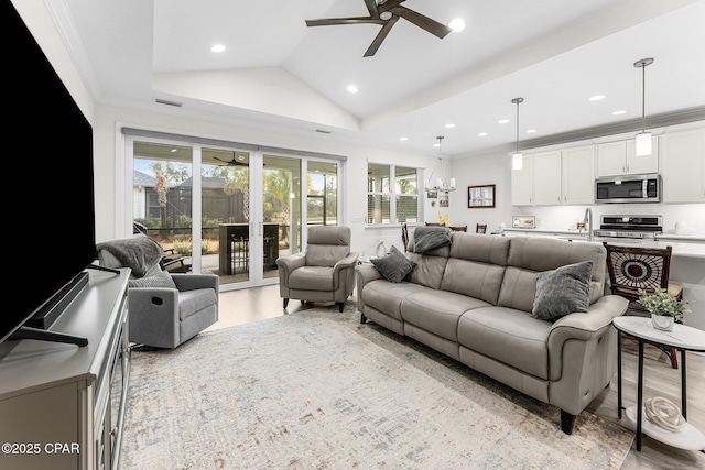 living room featuring vaulted ceiling, light wood-type flooring, ceiling fan with notable chandelier, ornamental molding, and sink